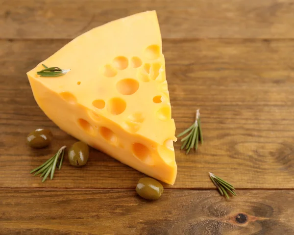 Кусок сыра с зелеными оливками, на деревянном фоне — стоковое фото