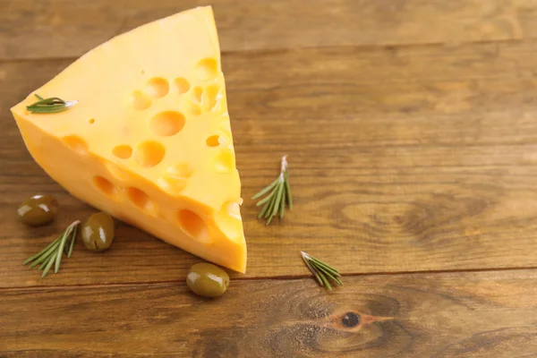 Кусок сыра с зелеными оливками, на деревянном фоне — стоковое фото