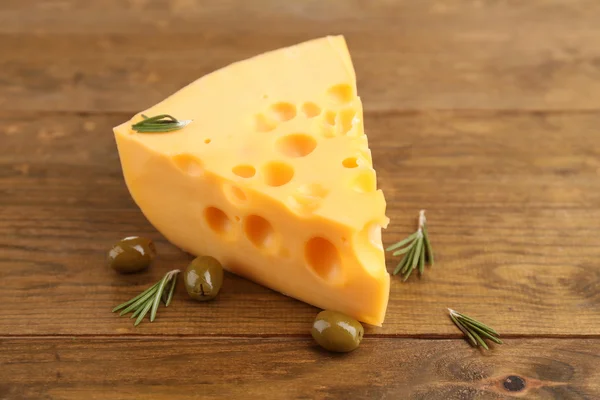 Pieza de queso con aceitunas verdes, sobre fondo de madera — Foto de Stock