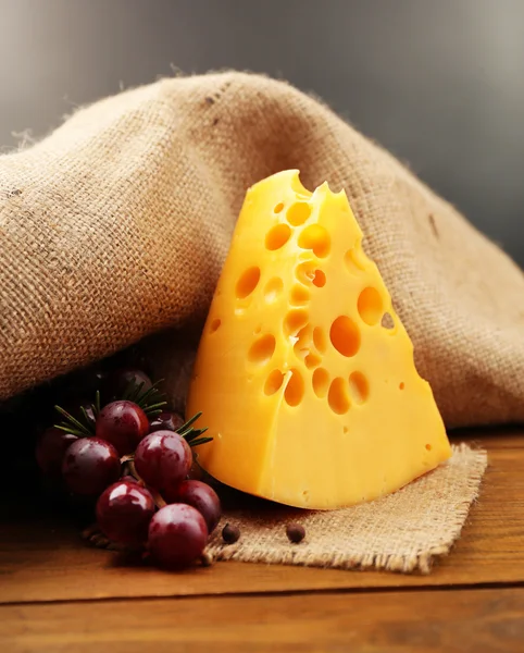 Piece of cheese on plate with green olives, on wooden table, on dark background — Stock Photo, Image