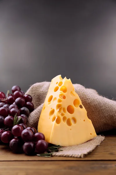 Pedaço de queijo com uva e alecrim sobre mesa de madeira, sobre fundo escuro — Fotografia de Stock