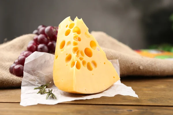 Pezzo di formaggio con uva e rosmarino sul tavolo di legno, su sfondo scuro — Foto Stock