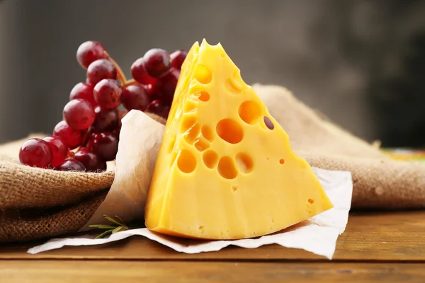 Piece of cheese with grape and rosemary on wooden table, on dark background — Stock Photo, Image