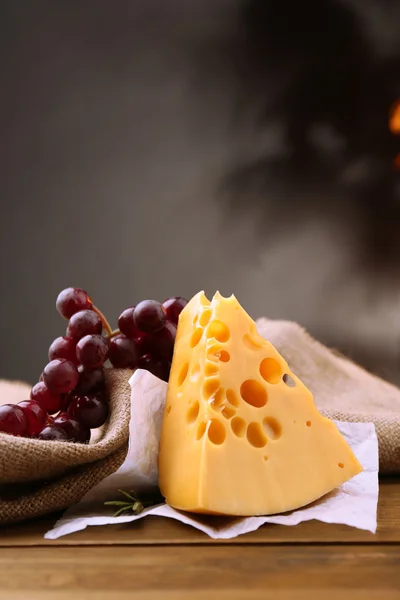 Pezzo di formaggio con uva e rosmarino sul tavolo di legno, su sfondo scuro — Foto Stock