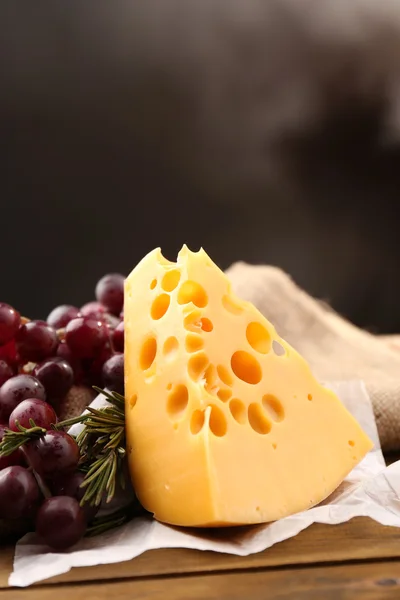 Käsestück mit Trauben und Rosmarin auf Holztisch, auf dunklem Hintergrund — Stockfoto