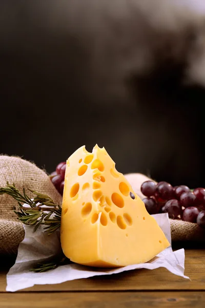 Käsestück mit Trauben und Rosmarin auf Holztisch, auf dunklem Hintergrund — Stockfoto