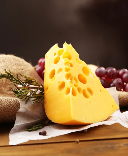 Шматок сиру з виноградом і розмарином на дерев'яному столі, на темному фоні — стокове фото