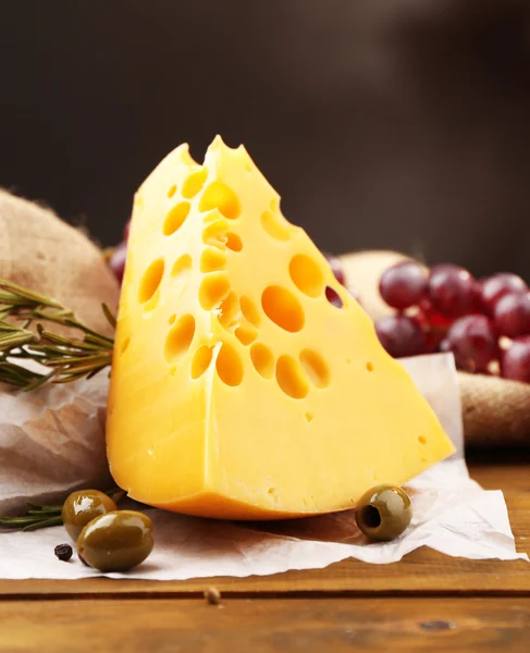 Pedaço de queijo em prato com azeitonas verdes, sobre fundo de madeira — Fotografia de Stock