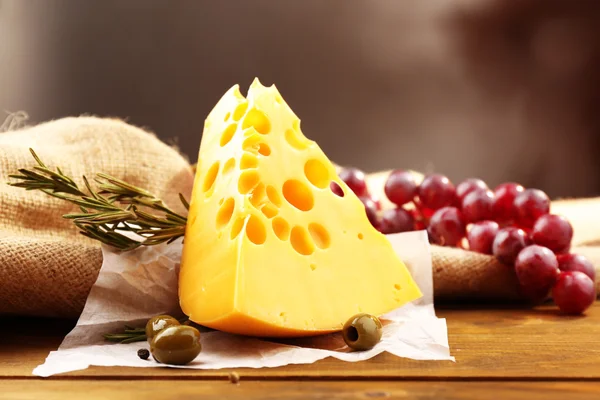 Шматок сиру на тарілці з зеленими оливками на дерев'яному фоні — стокове фото