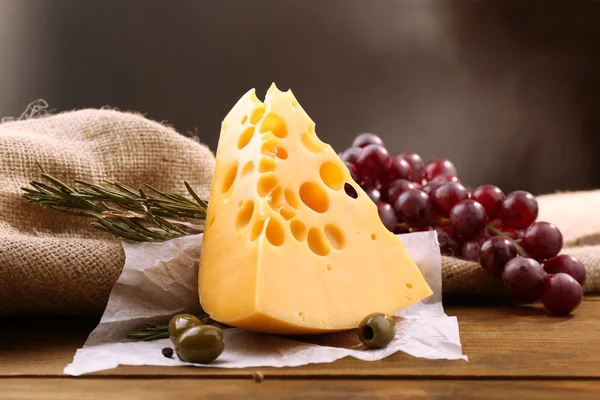 Piece of cheese on plate with green olives, on wooden background — Stock Photo, Image