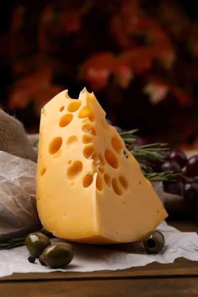 Кусок сыра на тарелке с зелеными оливками, на деревянном фоне — стоковое фото