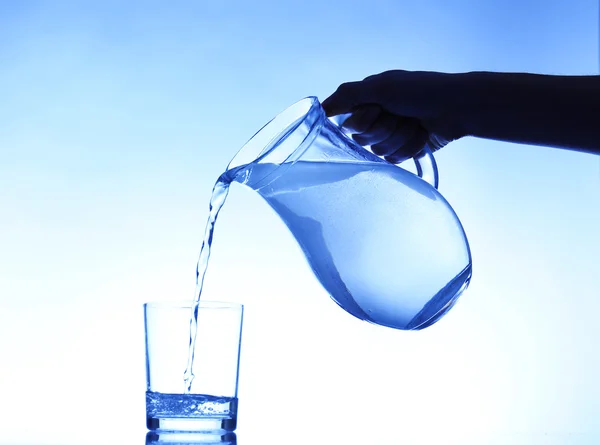 Despeje água do jarro em vidro, no fundo azul escuro — Fotografia de Stock