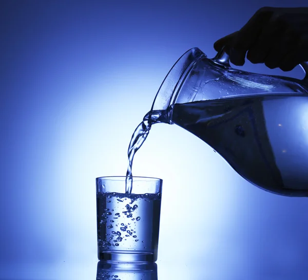 Verser l'eau du pichet dans le verre, sur fond bleu foncé — Photo