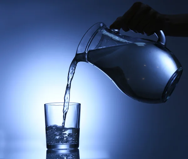 Pour water from pitcher into glass, on dark blue background — Stock Photo, Image