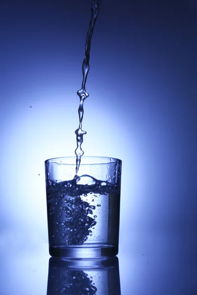 Versare l'acqua dalla brocca in vetro, su fondo blu scuro — Foto Stock