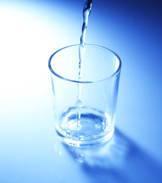 Vierta el agua de la jarra en un vaso, sobre un fondo azul oscuro — Foto de Stock