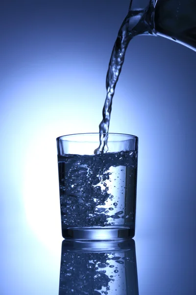 Pour water from pitcher into glass, on dark blue background — Stock Photo, Image