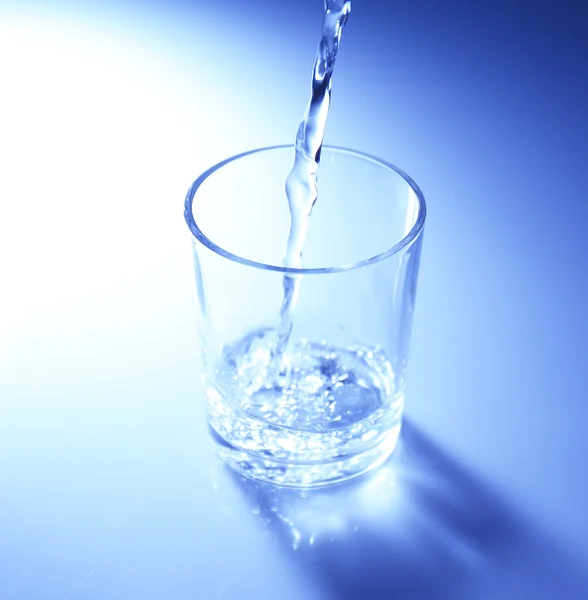 Vierta el agua de la jarra en un vaso, sobre un fondo azul oscuro — Foto de Stock