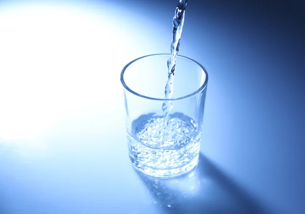 Vierta el agua de la jarra en un vaso, sobre un fondo azul oscuro — Foto de Stock