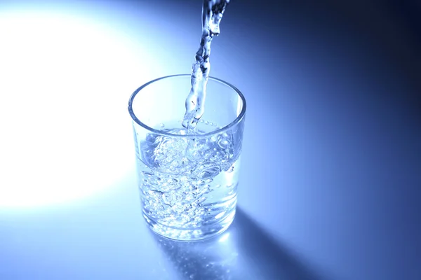 Häll vatten från kannan i glas, på Mörkblå bakgrund — Stockfoto