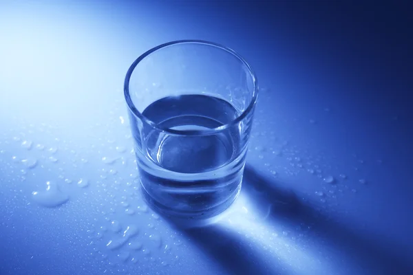 Acqua in vetro, su fondo blu scuro — Foto Stock