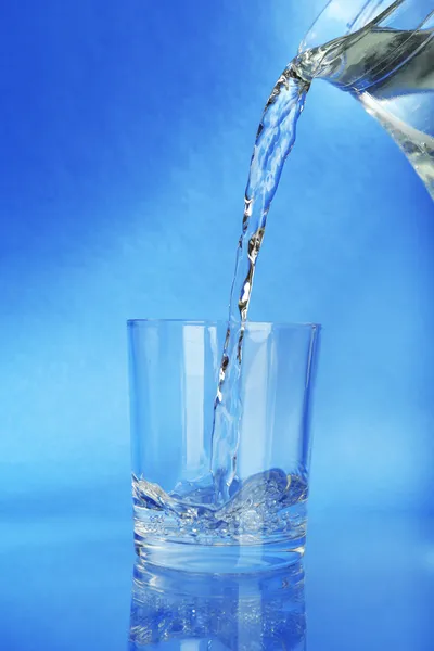 Ρίχνουμε νερό από την κανάτα σε ένα ποτήρι, σε σκούρο μπλε φόντο — Φωτογραφία Αρχείου