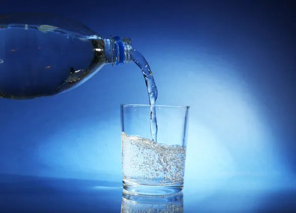 Vierta el agua de la botella en vidrio, sobre fondo azul oscuro — Foto de Stock