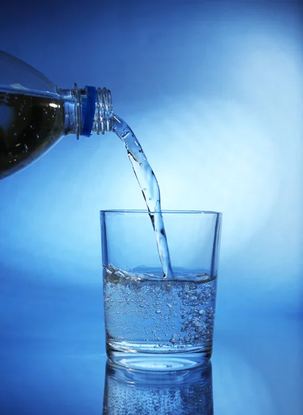 Tuangkan air dari botol ke kaca, pada latar belakang biru tua — Stok Foto