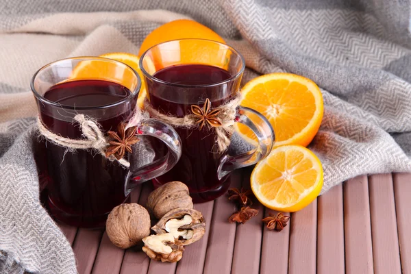Svařené víno s pomeranče a ořechy na tabulce na pozadí tkaniny — Stock fotografie