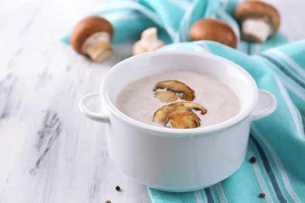 Mushroom soup in white pot, on napkin, on wooden background — Stock Photo, Image