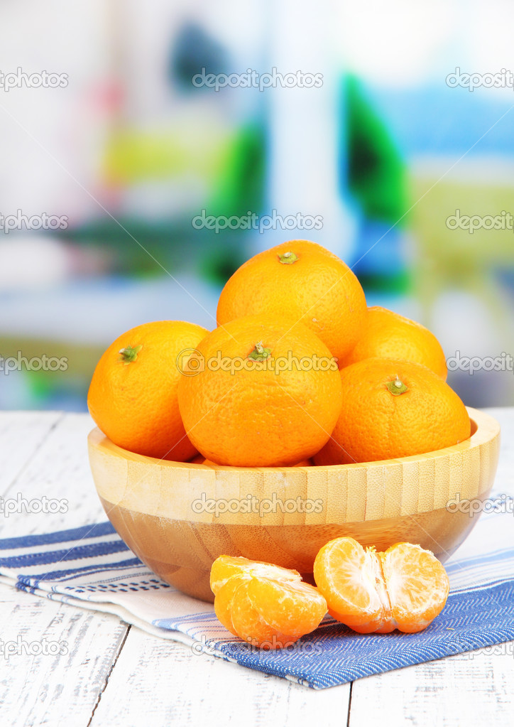 Ripe sweet tangerines with spices in bowl, on napkin, on bright background