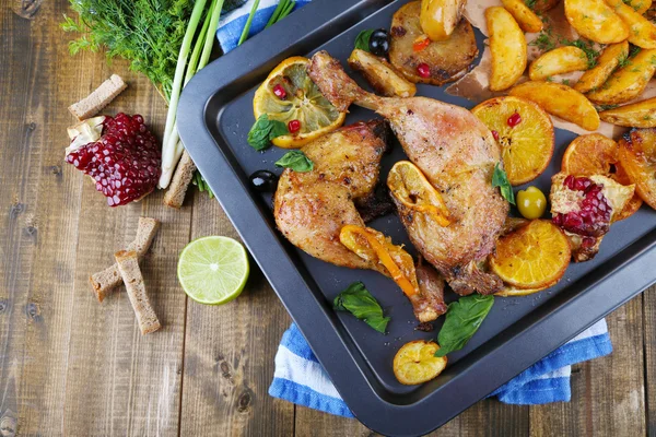 Homemade roasted chicken drumsticks with fried potatoes and vegetables on pan, on wooden background — Stock Photo, Image