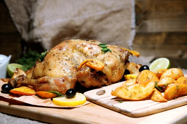 Whole roasted chicken with vegetables and fried potatoes on wooden board, on wooden background — Stock Photo, Image