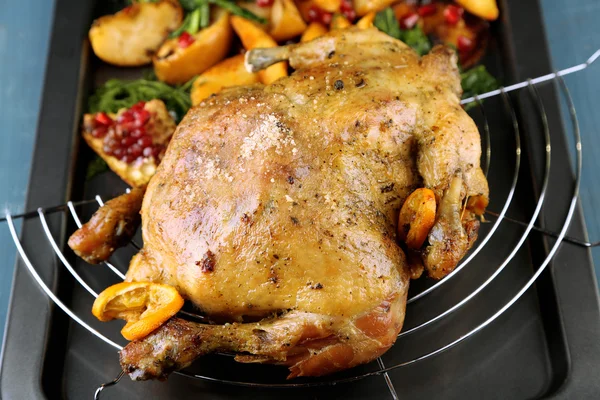 Целый жареный цыпленок с овощами и жареным картофелем на сковороде, на фоне цвета дерева — стоковое фото