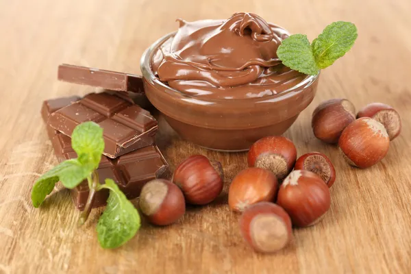 Sweet chocolate hazelnut spread with whole nuts and mint on wooden background — Stock Photo, Image