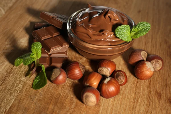 Sweet chocolate hazelnut spread with whole nuts and mint on wooden background — Stock Photo, Image