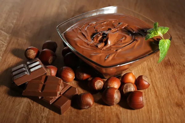 Zoete chocolade hazelnoot verspreid met hele noten en munt op houten achtergrond — Stockfoto