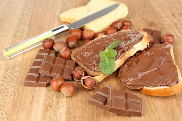 Pão com avelã de chocolate doce espalhado no fundo de madeira — Fotografia de Stock