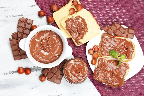 Avelã de chocolate doce espalhada com nozes inteiras e hortelã em fundo de madeira — Fotografia de Stock