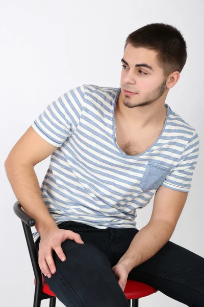 Handsome young man sitting on chair on light background — Stock Photo, Image