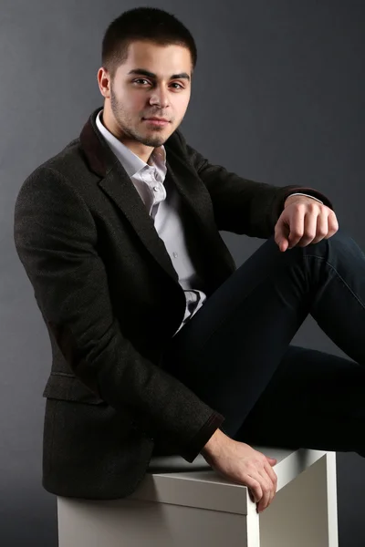 Handsome young sitting on cube on dark background — Stock Photo, Image