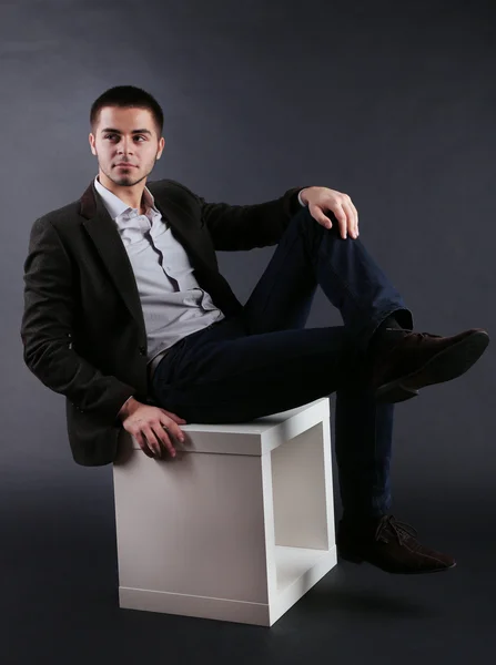 Guapo joven sentado en cubo sobre fondo oscuro —  Fotos de Stock