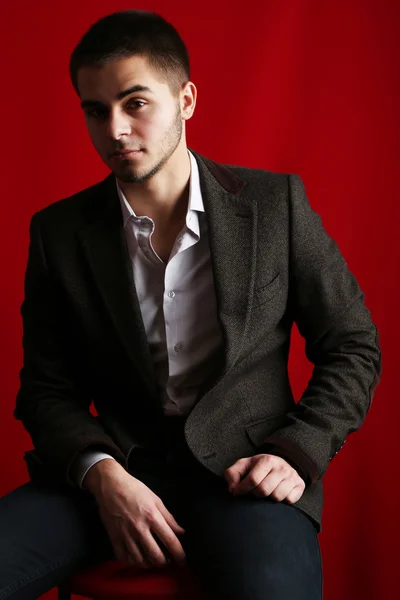 Handsome young sitting on chair on red background — Stock Photo, Image