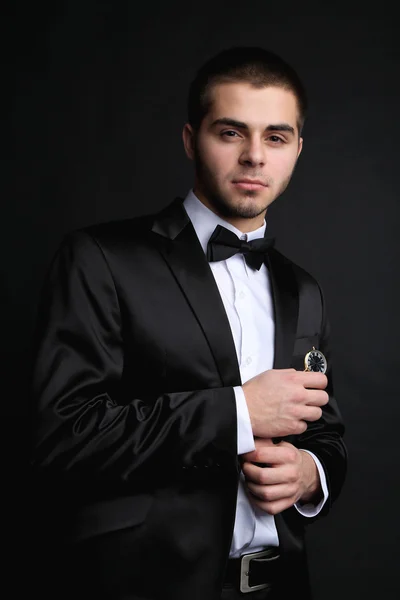 Handsome young man in suit holding watch on dark background — Stock Photo, Image