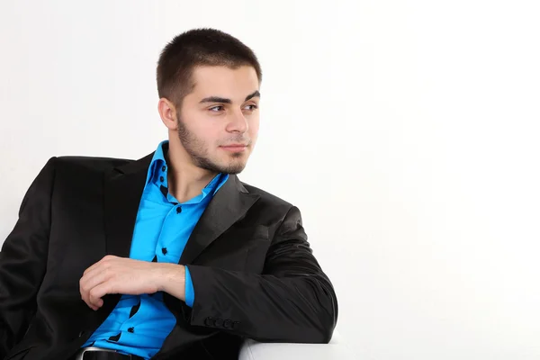 Handsome young man sitting on sofa on light background — Stock Photo, Image