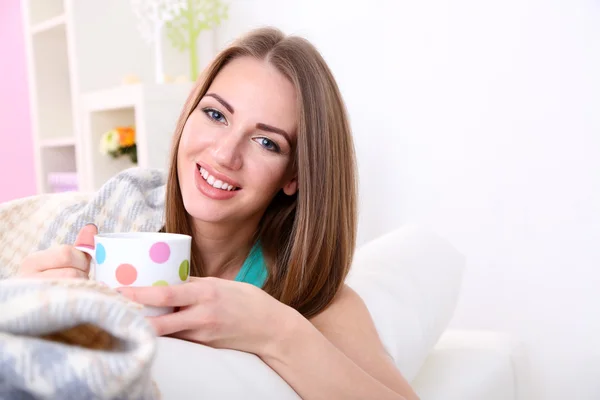 Young woman resting with cup of hot drink on sofa at home — Stock Photo, Image