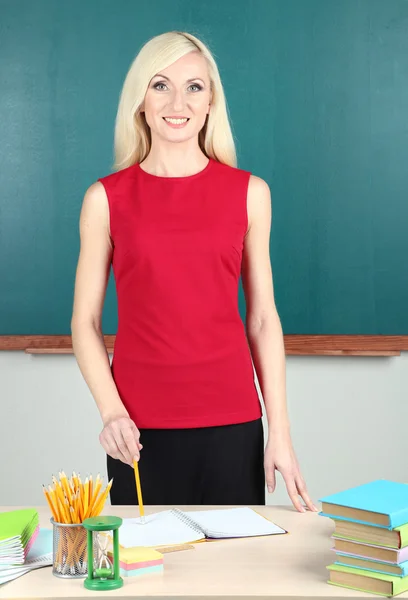 School teacher near table on blackboard background — Stock Photo, Image