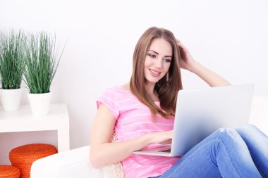 Evdeki kanepede dizüstü bilgisayarıyla dinlenen genç bir kadın.