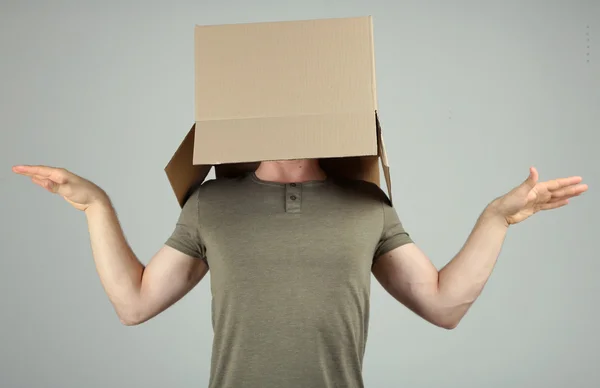 Человек с картонной коробкой на голове на сером фоне — стоковое фото