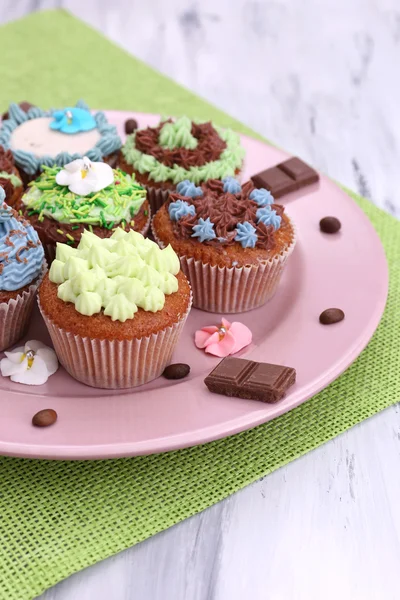 Leckere Cupcakes mit Buttercreme, auf Teller, auf Farbserviette, auf Farbholzhintergrund — Stockfoto